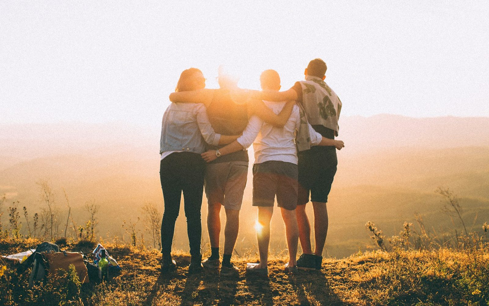 four person hands wrap around shoulders while looking at sunset